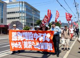 関西電力原子力事業本部(左奥)周辺で行進する市民団体=30日午後、福井県美浜町