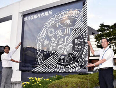 東邦銀行川俣支店入り口のアーチに掲げられたタペストリーを披露する樋口支店長（右）