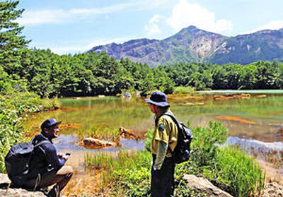 磐梯山を望む銅沼で一休みしながら、小野寺さんから話を聞く記者（左）