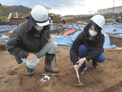 上田さん（左）の指導の下、慎重に土の表面を削る記者