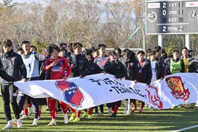 試合後、「チカラをひとつに。―ＴＥＡＭ　ＡＳ　ＯＮＥ―」と書かれた横断幕を持ち、サポーターに手を振るいわきと福島の選手たち＝１８日、広野町・Ｊヴィレッジスタジアム