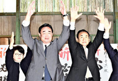 ４選を果たし万歳で喜ぶ松本氏（中央）。左は妻美智代さん