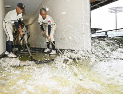 一時強い雨が降り、一塁ベンチが浸水し、水をかき出す福島東高の選手。開幕試合は雨天順延となった＝１２日正午、あづま球場