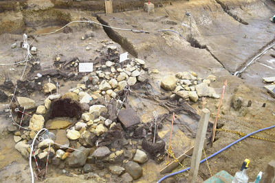 発見された奈良時代の水場遺構。左側にある木組みの井戸枠状の遺構から右側にかけて段状になっている。白色の紙がある場所は木簡の出土地点＝西久保遺跡