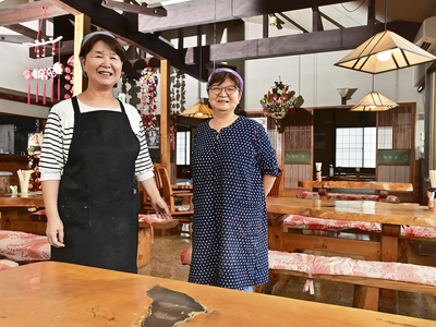 店に立つみどりさん（左）と美喜子さん。父の久さんが手がけたケヤキのテーブルは今も現役。落ち着いた雰囲気で来店客をもてなしている（吉田義広撮影）