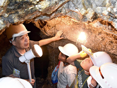 坑道跡に入り、相田さん（左）から石川町の鉱山の歴史や鉱石について学ぶ児童＝石川町・和久観音山鉱山跡