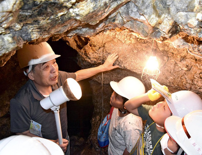 坑道跡に入り、相田義男さん（左）から石川町の鉱山の歴史や鉱石について学ぶ児童＝石川町・和久観音山鉱山跡