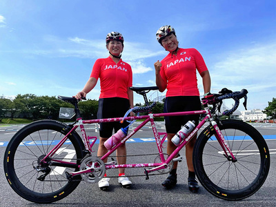 競技用タンデム（２人乗り自転車）の前で写真を撮る私たち。コロナ禍でパラリンピックが延期になっても、開催を信じて練習した