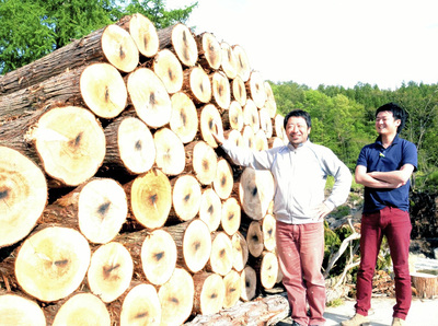 山積みされた認証森林材の利活用促進を誓う私。ＮＰＯ法人の事務局を務めていた松沢瞬さん（右）と協力して要望活動などを進めた＝２０１６年５月