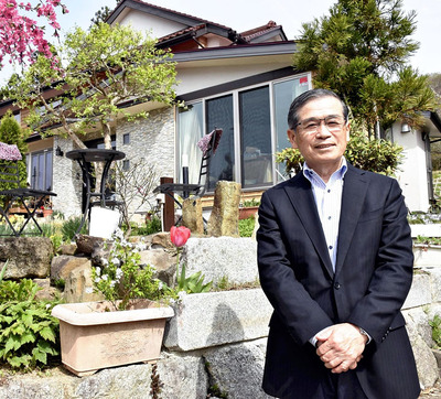 妻と２人で住む自宅を背にする私。これまでの人生、実に多くの出会いや出来事があった。苦楽を共にした古里への愛情を持ち続け、残りの人生も豊かなものにしていきたい