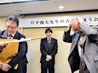 教え子から「金のトング」と軍手、ビニール袋をもらい、思わず頭を抱える私（右）。年老いても元気づくりに励めというユーモアのある計らいにうれしさが募る。授与者は日本パラ陸連強化委員長の宍戸英樹君＝２０１４年