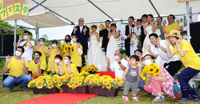 ヒマワリ畑での結婚式で写真撮影する人たち。ヒマワリを通じた縁がカップルを祝福する笑顔につながった