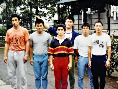 レスリング部の合宿所（右奥）を前に、中央で手を上げているのが私。当時の生活に戻りたくはないが、仲間と集まって飲むと合宿所の思い出話に花が咲くから不思議だ