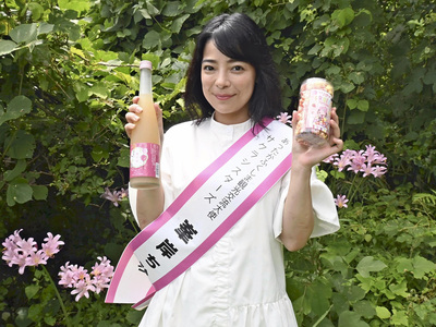 事務所の敷地内でポーズを取る私。県産モモを使ったお酒やカラフルなポップコーンは日台で人気で、商品販売に手応えを感じている