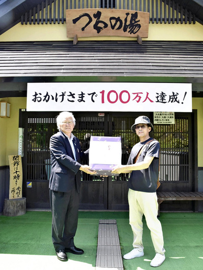 つるの湯入湯者１００万人達成時の式典の様子。矢沢源成町長（左）が１００万人目の入湯者に記念品を渡している