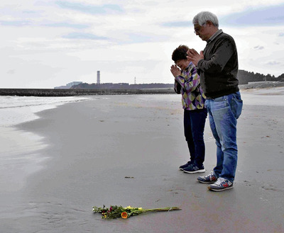 海に花を手向け、手を合わせる友良さん（手前）と聡子さん夫妻＝富岡町