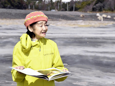 海に向かって絵本の読み聞かせをする梶田さん。海に問いかけるようにページをめくった＝南相馬市・北泉海岸