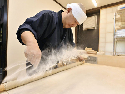 甚平に鉢巻き姿でそばを打つ林さん