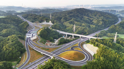 朝日に照らされる復興再生道路「小名浜道路」。いわき市の小名浜港と右上から通る常磐道を結ぶ小名浜道路は８月７日午後３時に開通する。物流の円滑化や観光の活性化が期待される＝いわき市山田町・いわき小名浜インターチェンジ付近（ドローン撮影）