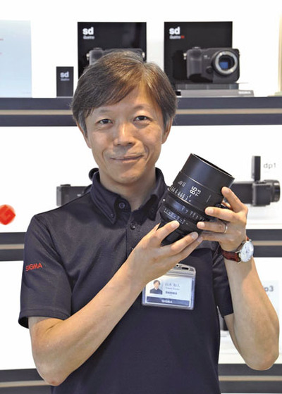 ハリウッド映画「トップガン　マーヴェリック」の撮影で使用されたレンズを手にして取材に応じる私。ハリウッドの映画製作者からもシグマの高い技術力が認められた＝２０１９年