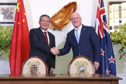 　１３日、ニュージーランドの首都ウェリントンで握手するラクソン首相（右）と中国の李強首相（ゲッティ＝共同）