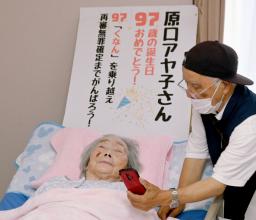 　９７歳の誕生日に県外の家族と電話する原口アヤ子さん。右は支援者の武田佐俊さん＝１５日午後、鹿児島県の介護施設