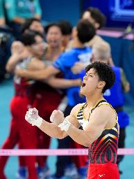 　男子団体総合決勝　最終種目の鉄棒で着地を決めガッツポーズの橋本大輝。奥は喜ぶ日本チーム＝２９日、パリ（共同）