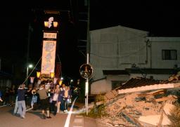 　石川県輪島市町野町曽々木地区の夏祭り「曽々木大祭」が開かれ、地震で被害を受けた建物の前を進む巨大な灯籠「キリコ」＝１７日夜