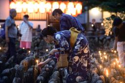 　化野念仏寺で始まった「千灯供養」で、石仏にろうそくをともす参拝者＝２４日夕、京都市