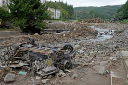 　記録的豪雨で氾濫した塚田川沿いで、ひっくり返ったまま残る車＝２０日午前、石川県輪島市久手川町