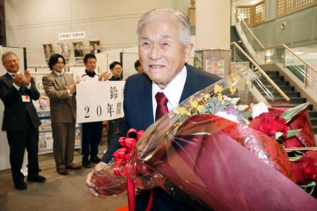 　退任で贈られた花束を手に笑顔で青森県田舎館村役場を後にする、現職首長で全国最高齢の鈴木孝雄村長＝１５日午後