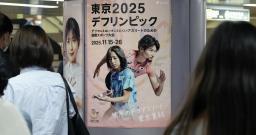 　聴覚障害者の国際スポーツ大会「デフリンピック」のポスターの前を行き交う人たち＝１４日午後、東京都港区