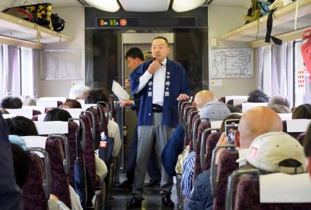 　長野県内のＪＲ飯田線を走る特別列車で、乗客に伊那地域の酒について説明する地元の酒造関係者＝２５日午後